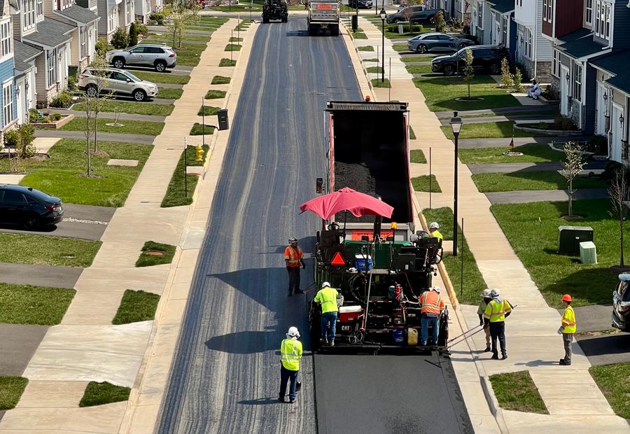 Paving crew running a CAT paver down an Erie street, laying hot mix behind it