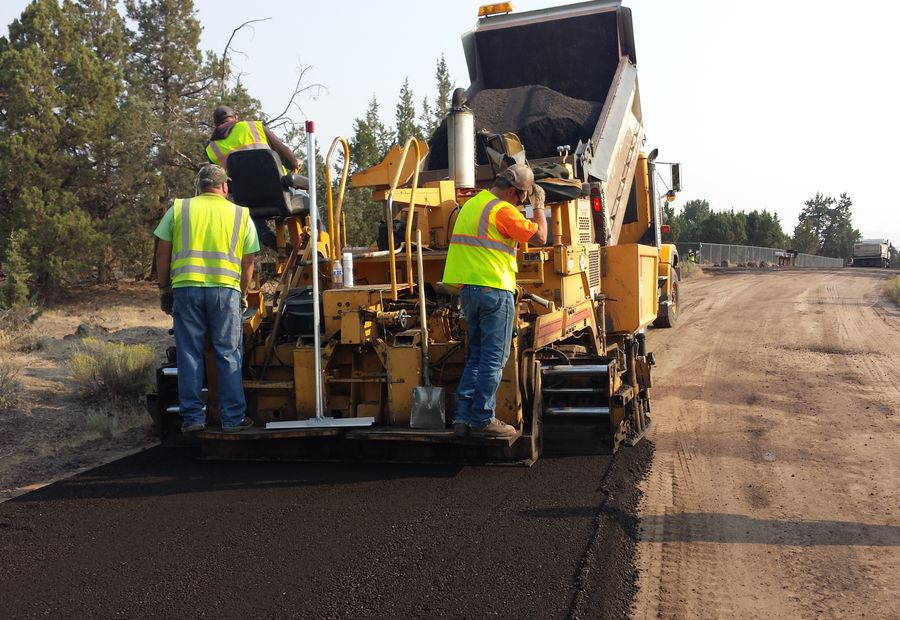 Crew riding the paver as it lays asphalt over a fresh gravel base