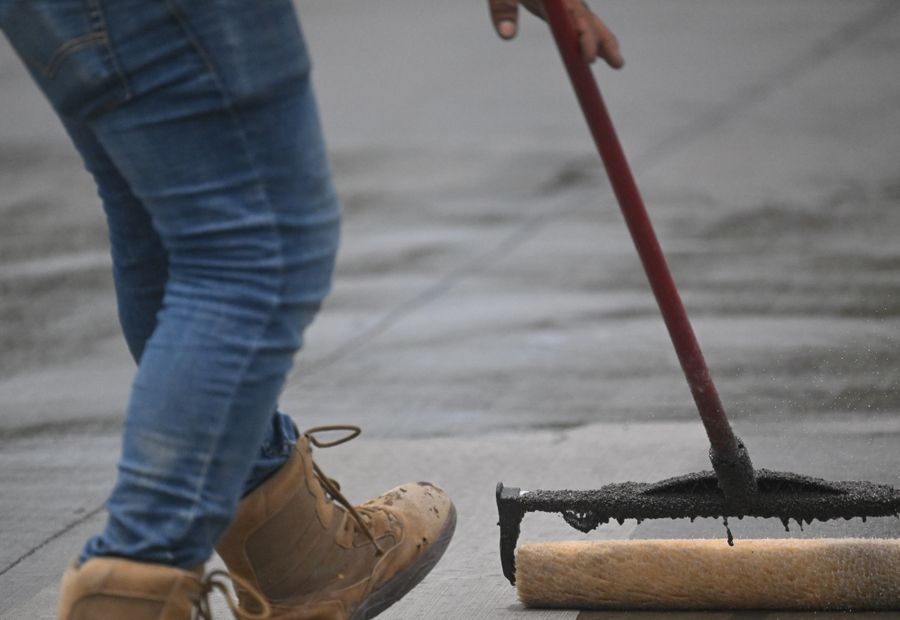 Worker pulling a squeegee of black sealer in an even band across a driveway